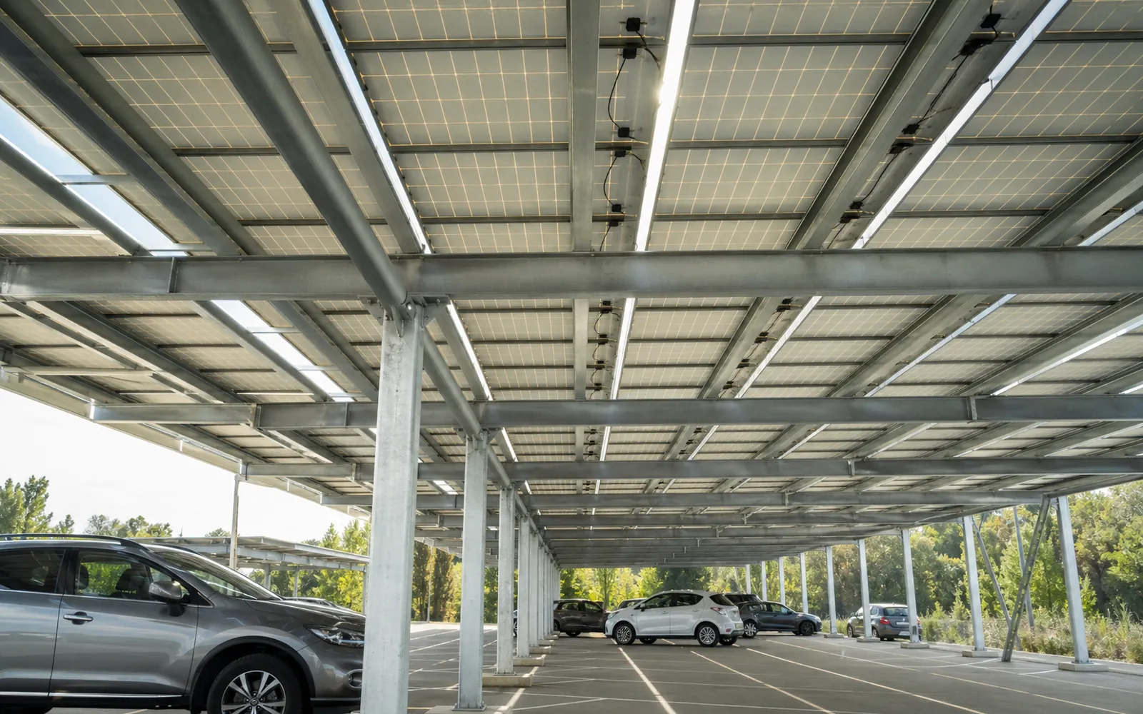 Dessous d’une ombrière photovoltaïque de parking, panneaux et structure en acier au-dessus des voitures